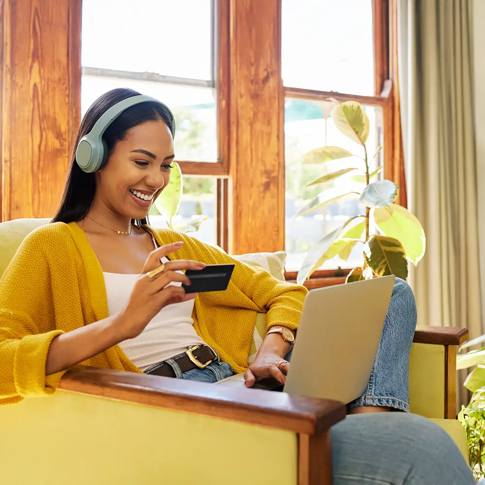 Woman shopping online from home using a laptop and holding a credit card.