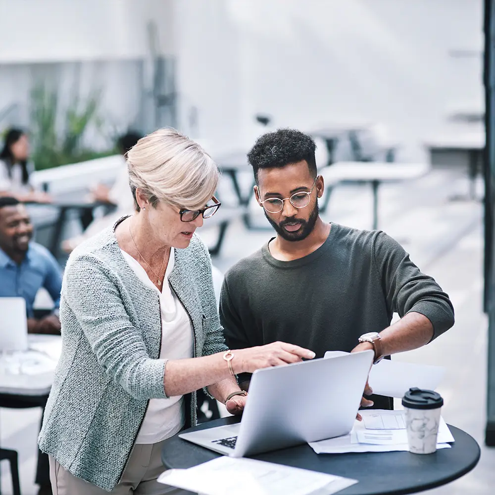 Two professionals reviewing financial information together on a laptop at an outdoor workspace.