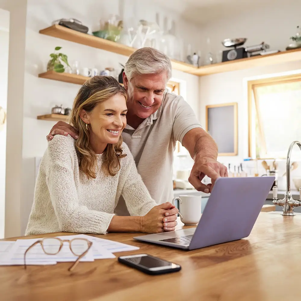 Senior couple using a laptop at home while reviewing insurance documents together.